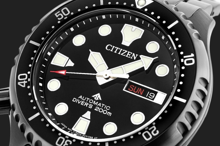 Czarna tarcza zegarka CITIZEN NY0145-86E z fluorescencyjnymi indeksami i wskazówkami.